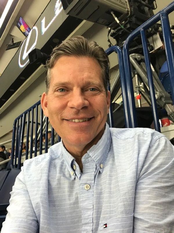 A smiling man in a light blue button-up shirt at an indoor event.
