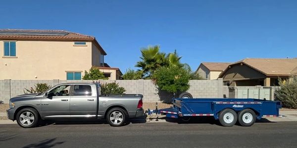 A grey pickup truck towing a blue trailer in the street lot on a sunny day.