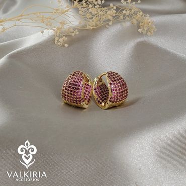 Gold earrings studded with purple gems on silver fabric.
