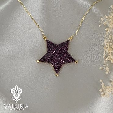 Gold necklace with a sparkling purple star pendant on a silky background.