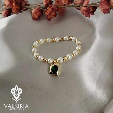 Elegant pearl and gold bracelet with green gemstone charm on satin.