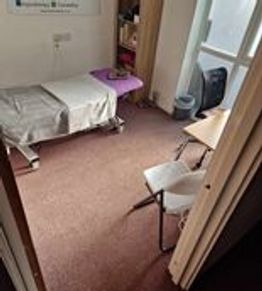 A small, simple medical examination room with a bed and chairs.