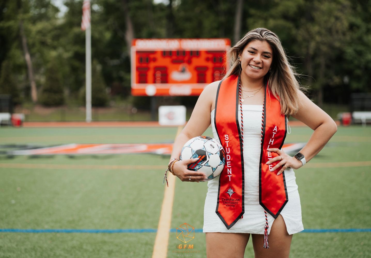 Graduate student athlete holding a soccer ball on a sports field.