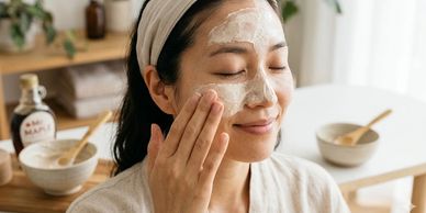 Woman applying a creamy facial mask with a headband in a cozy room.