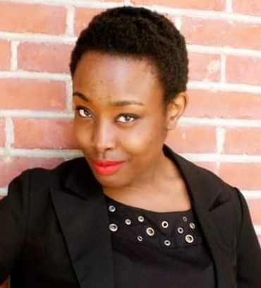 Wangane Hall. A young stylish black woman smiles in front of a brick wall.