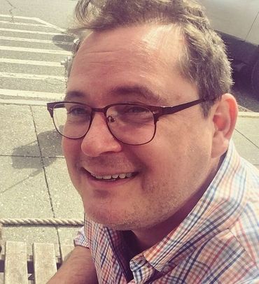 Jason Lemiuex. A mid-aged white man with short brown hair. glasses,  and checked shirt smiles from a