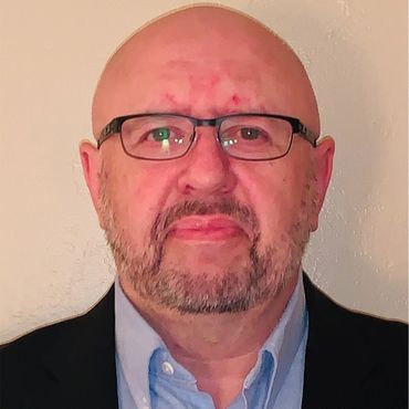 Billy Ryan, an Irish looking white man with a goatee,  glasses, suit, and smile.