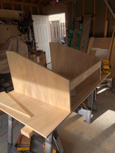 Wooden cabinet structure being assembled in a sunlit workshop.