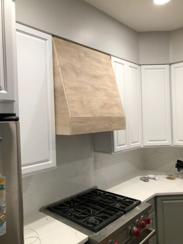 Modern kitchen with white cabinets and a wooden range hood above a stainless steel stove.