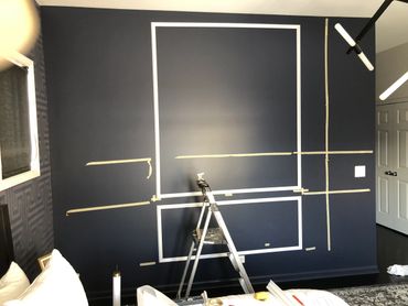 A dark blue wall with white taped rectangles and a ladder in front.