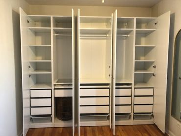 Open white wardrobe with multiple shelves and drawers in a room.