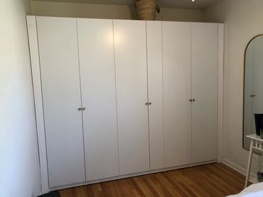 A large white wardrobe with multiple doors in a minimalist room.