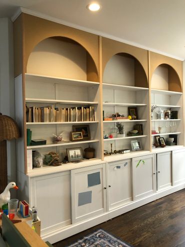 White built-in shelves with books, decor, and arched tops in a cozy room.
