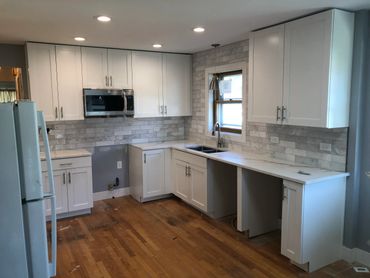 Modern kitchen with white cabinets, marble countertops, and tile backsplash under recessed lighting.
