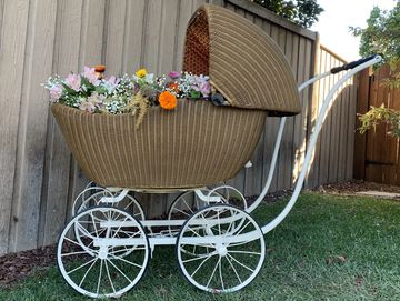 Vintage wicker baby carriage filled with colorful flowers in a garden.