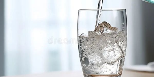 A glass being filled with sparkling water and ice cubes.