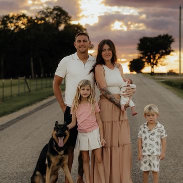 Family with three kids and a dog on a country road at sunset.