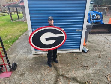 Man holding a large Georgia Bulldogs logo sign outdoors.