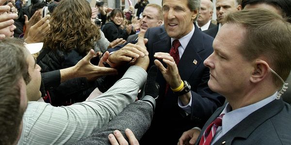 A politician shaking hands with a crowd while security watches closely.