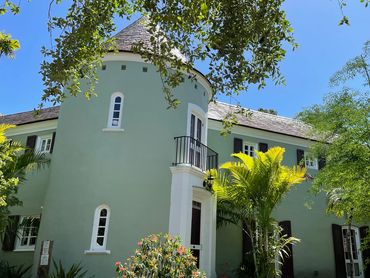 Charming green house with a turret and lush garden under a clear blue sky.