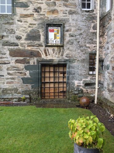 Old stone wall with a barred wooden door and a colorful crest above it.