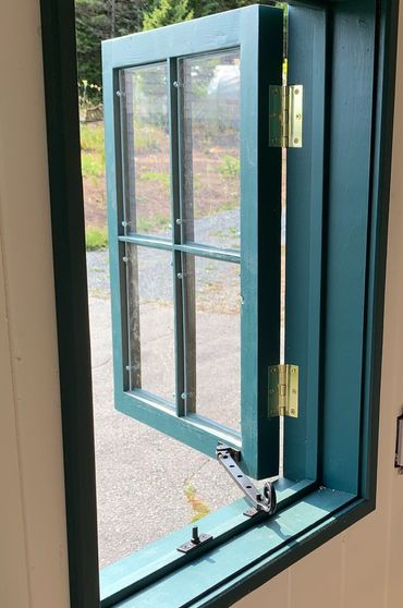 Open teal window with brass hinges and latch inside a room.