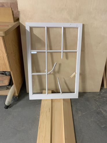 White window frame with broken glass and wooden slats in a workshop.