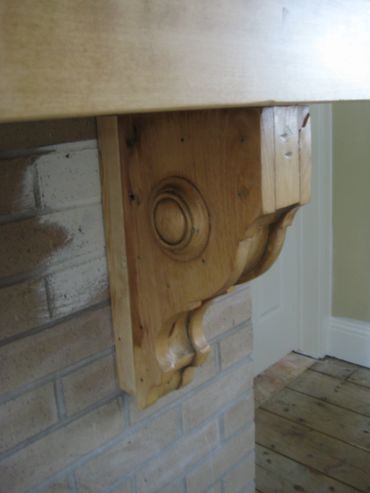 Decorative wooden corbel supporting a mantle over a brick fireplace.