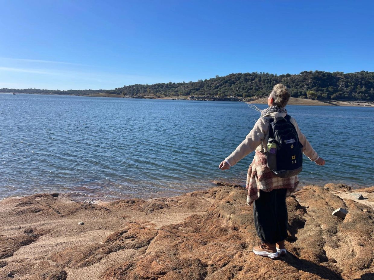 Person with backpack enjoying a scenic lakeside view on a sunny day.