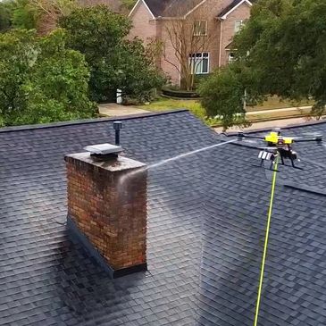 A residential building roof is being cleaned by a drone cleaning service. Roof cleaning power wash.