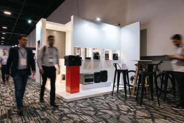 Stand blanco con exhibición de productos y mesas altas en una exposición