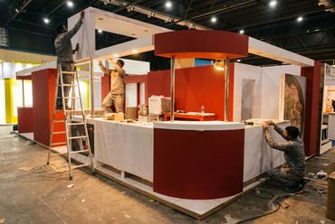 Armado de un stand con mostrador rojo y blanco antes de la apertura de la feria