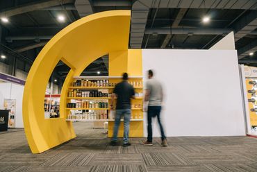 Stand con arco amarillo y estanterías de producto en una feria
