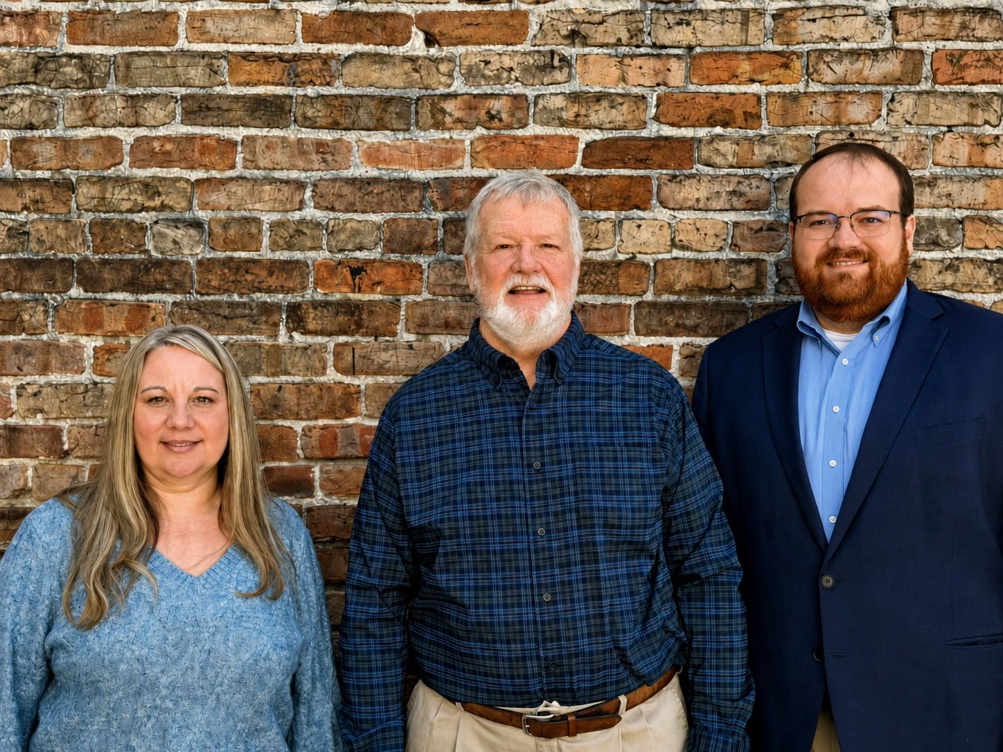 Three members of the Thad Glass Insurance team standing in front of a brick wall.