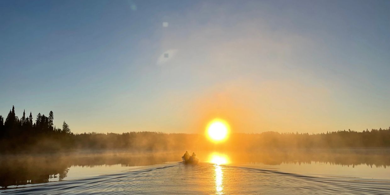 Boat with two people on a misty lake at sunrise.