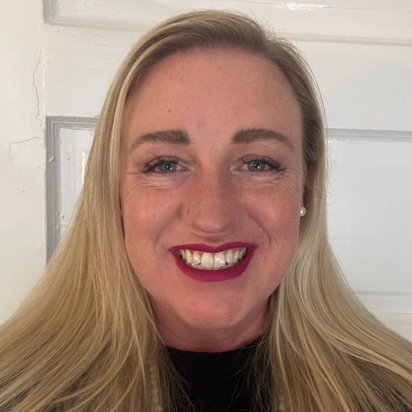 Smiling woman with blonde hair and bold lipstick against a white door.