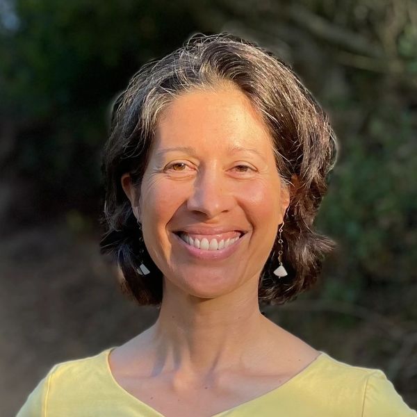 Smiling woman outdoors with short hair and yellow top.