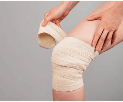 Person wrapping an elastic bandage around their knee for support.