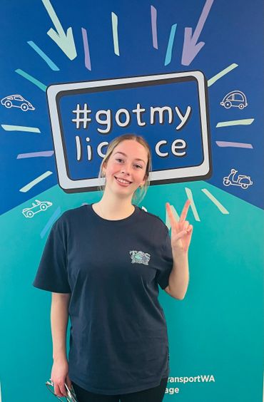 Young woman smiling and holding a peace sign in front of a colorful #gotmylicense sign.