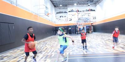 Kids playing basketball indoors on a court with orange and black walls.