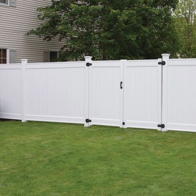 White vinyl privacy fence with gate in a green backyard.
