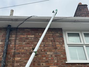 White pole attached to a brick house wall near a window and gutter. Gutter clearance