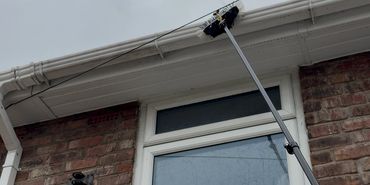 A brush on a long pole cleaning the gutter of a brick house.