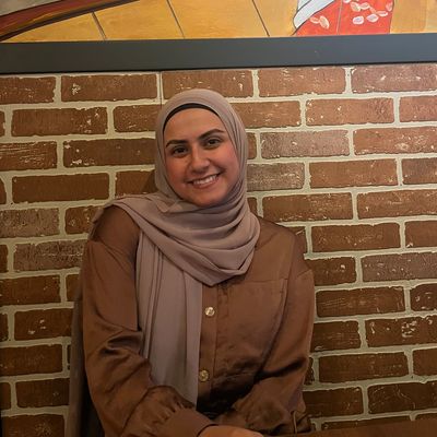 A smiling woman sitting against a brick wall with a colorful painting behind her.