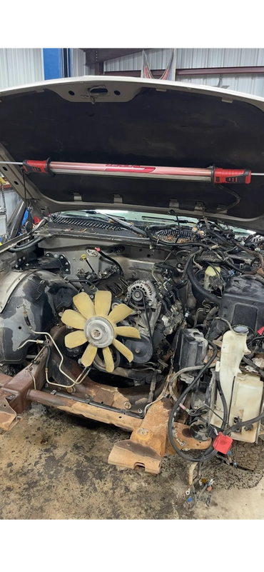 Car engine bay with parts removed and a work light attached to the hood.