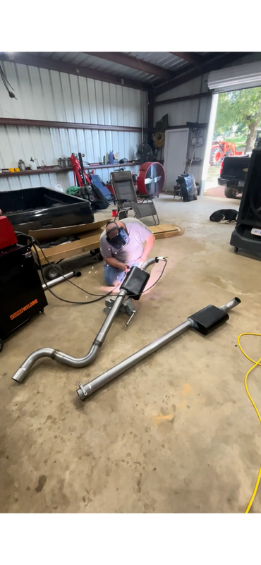Person welding car exhaust pipes in a spacious workshop.
