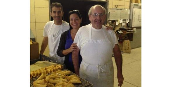 Three people smiling in a bakery with trays of pastries.