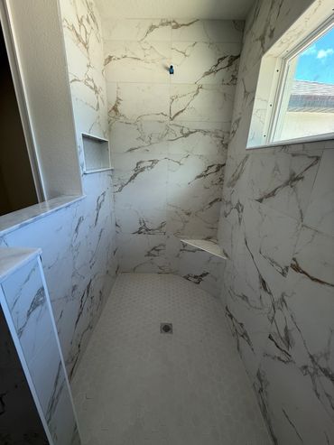 Modern shower with marble-patterned tiles and a small built-in bench.