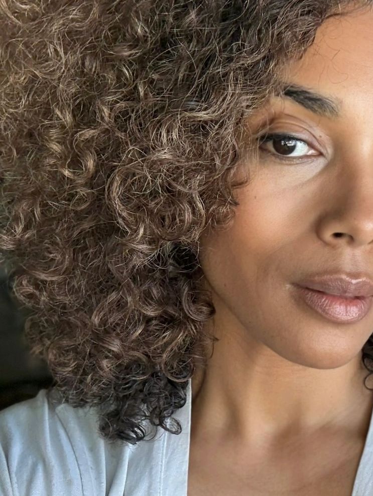 Close-up of a woman with curly hair and natural makeup.