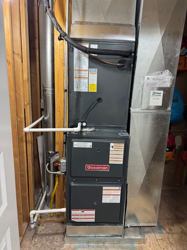 Goodman HVAC system installed in a utility area with pipes and ductwork.